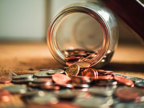 A savings jar of spilled over coins scattered on the floor